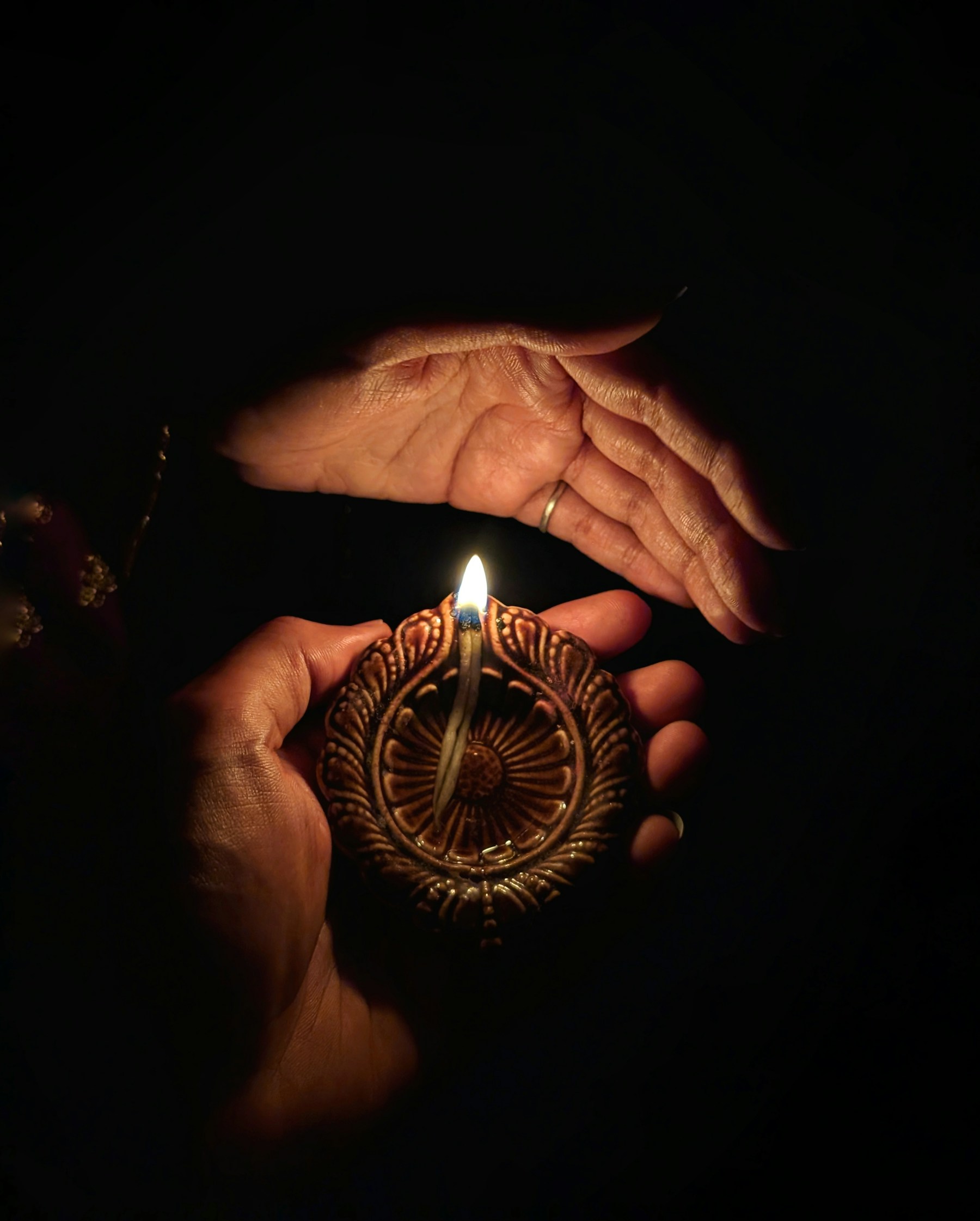 Hands gently sheltering the flame of a traditional clay lamp